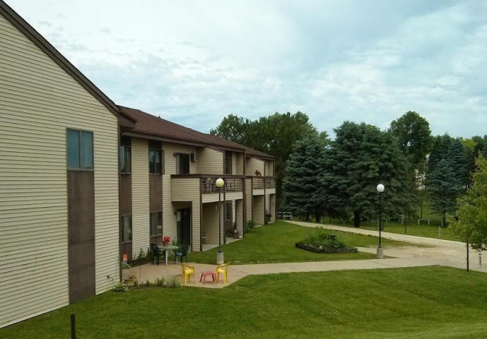 View of condo apartments with balconies and lawn with trees and light standards.