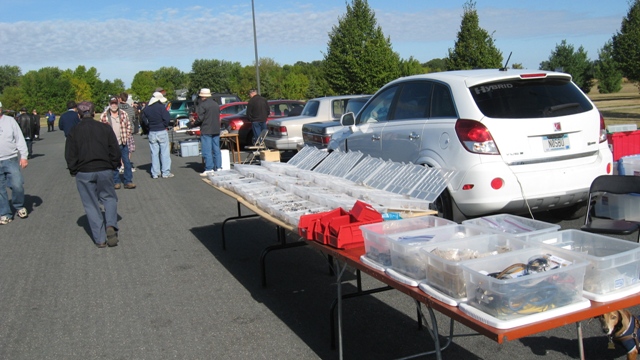 Outdoor swapmeet tables showing the Connectors by George inventory with PJ in the photo, hiding under the table in the lower right corner.