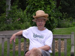 Pat sitting on bench, wearing stacked straw summer hats